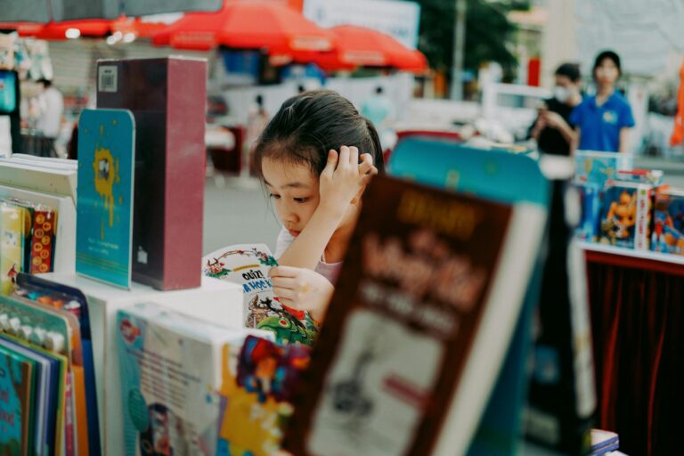 A young girl engrossed in a book at an outdoor book fair surrounded by colorful books and vibrant atmosphere.