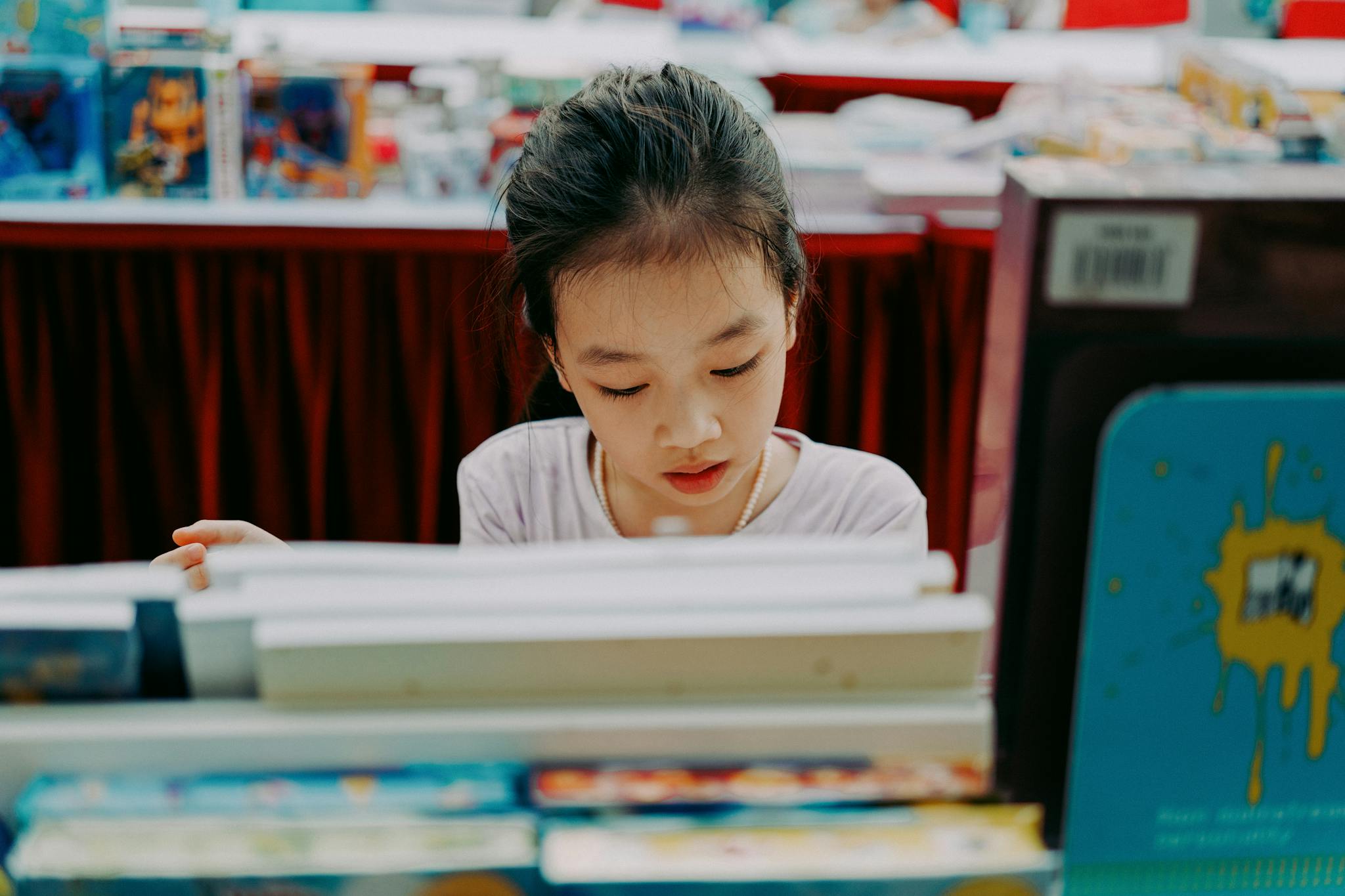 A young girl engrossed in books at a book fair, with colorful selections around her.