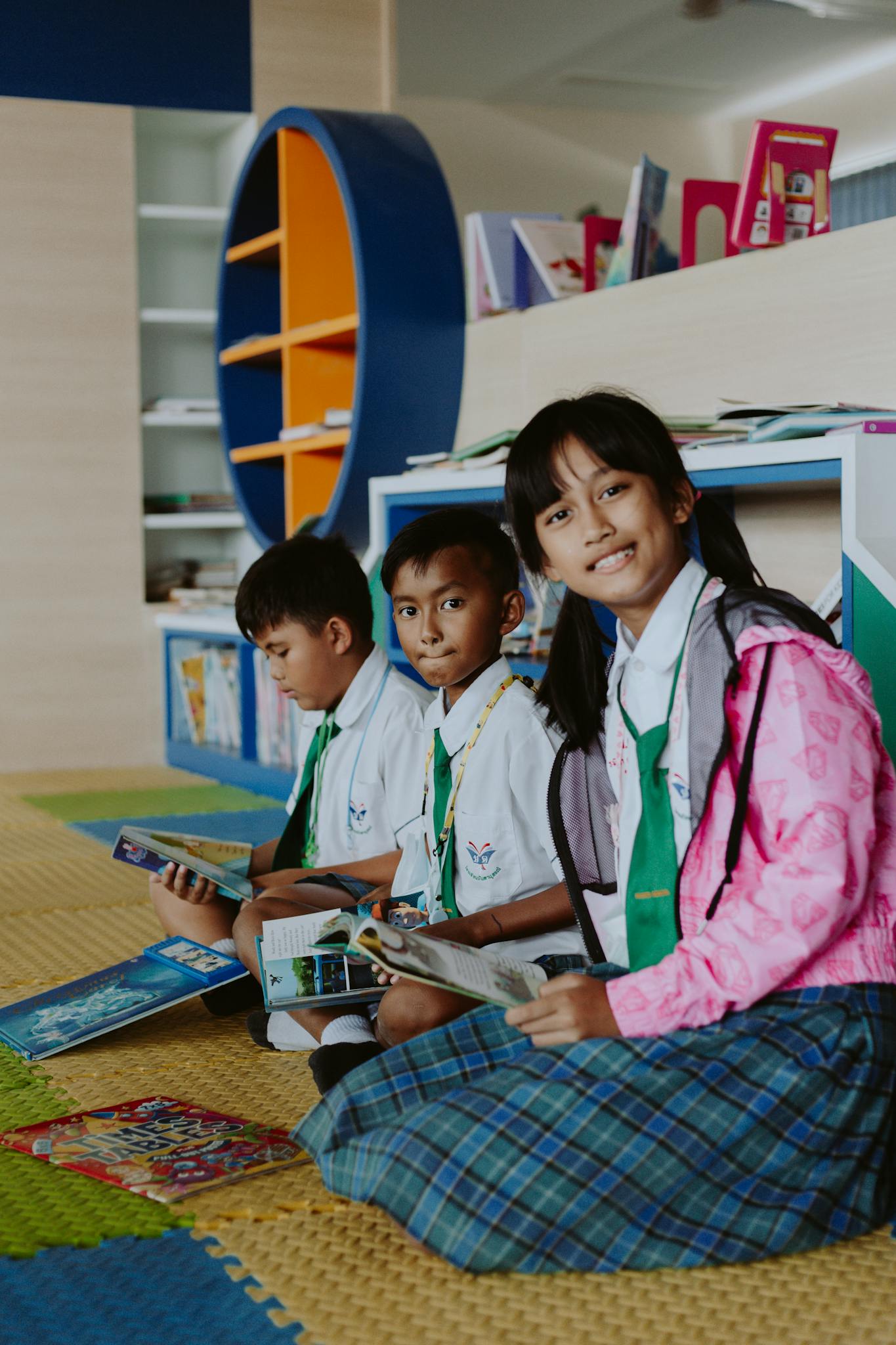 Three school children reading books in a modern library setting, promoting education and learning.