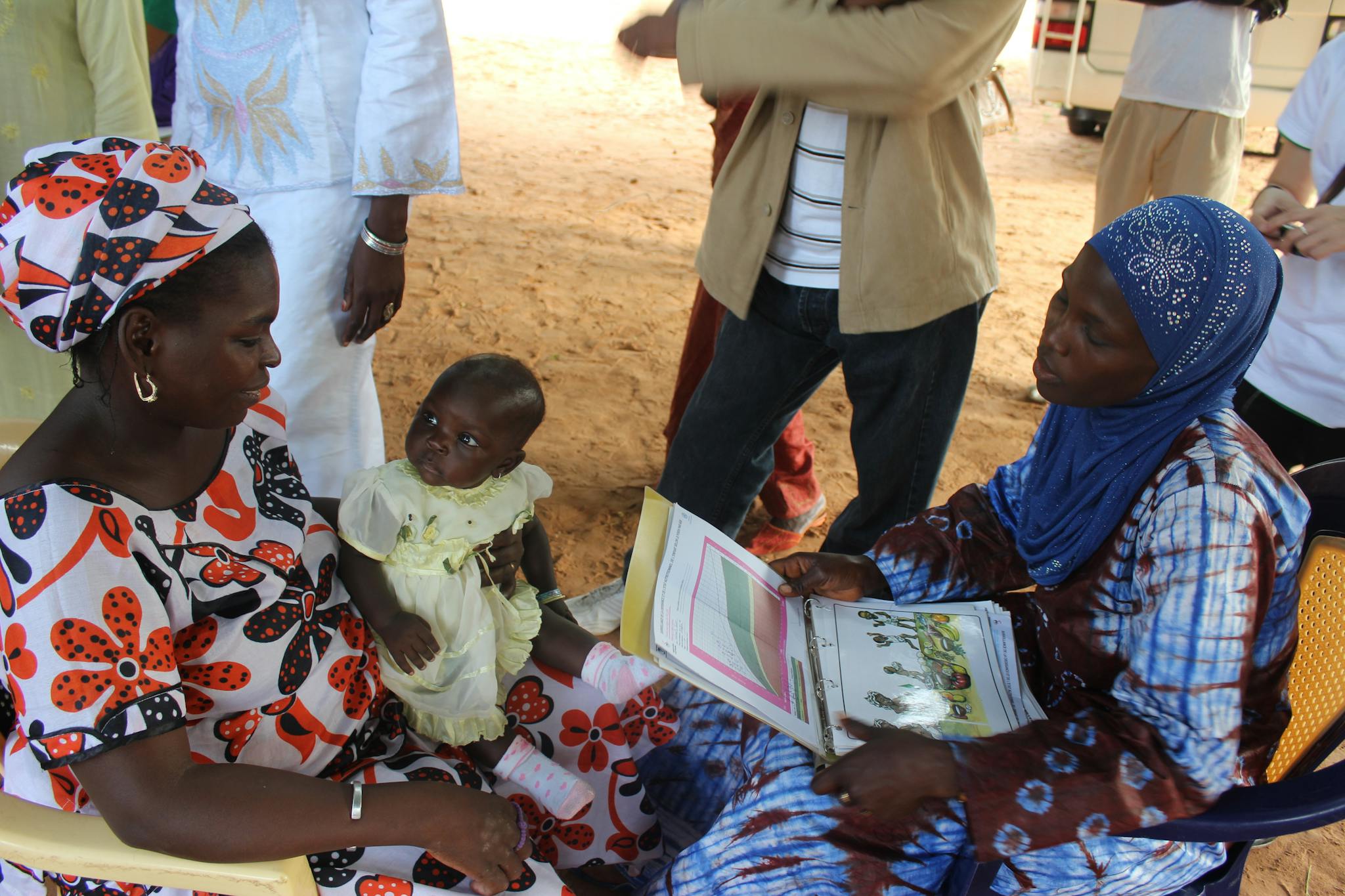 Two African women and a baby reading a book outdoors, fostering education and family bonding.